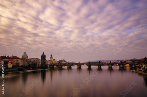 Beautiful sunrise near famous Charles Bridge with cloudy sky and water reflection. Bridge with amazing tower and old statues at early morning. Typical sunny day in Prague, Czech republic.