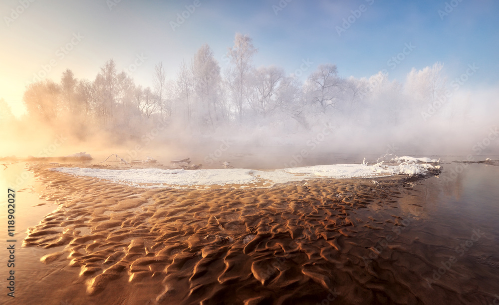 Winter landscape. Frosty, misty morning on the small river. Frost covered tree in the warm glow of sunrise on the beach. Misty sunrise at the forest river. The beauty of the world. Belarus