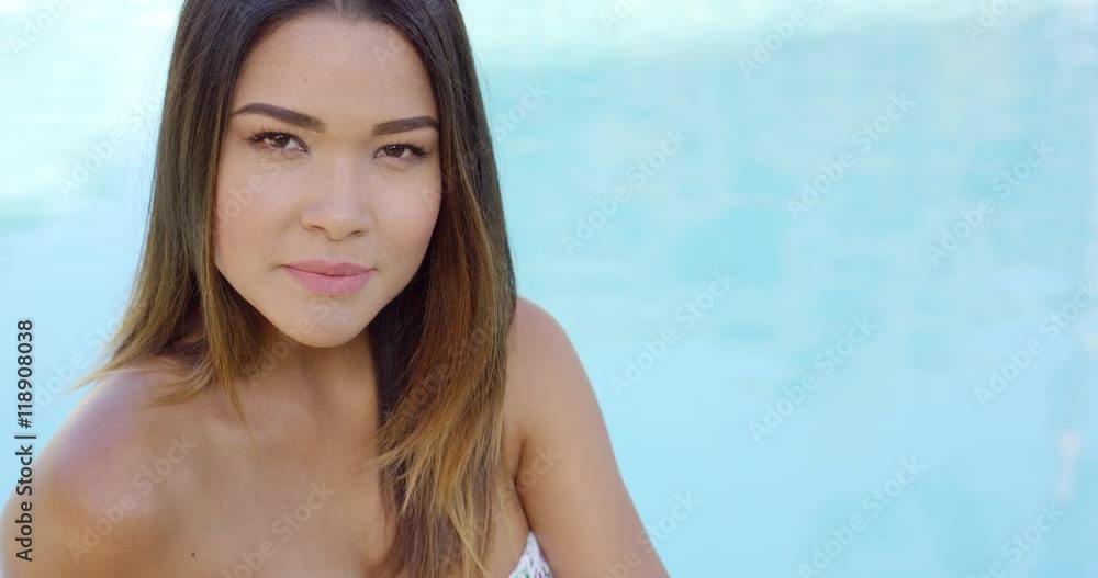 Attractive woman relaxing alongside a pool looking intently at the camera with a serious expression with copy space Attractive woman relaxing alongside a pool looking intently at the camera with a serious expression with copy space