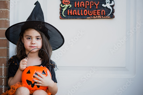 Pretty little girl in witch hat with pumpkin bag looking at camera photo
