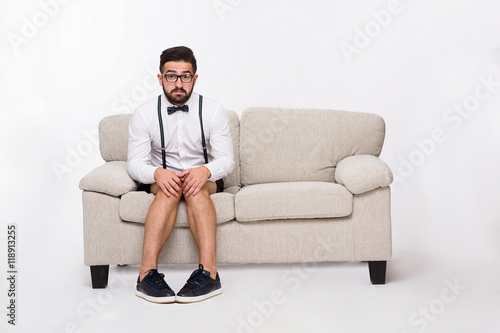 Picture of frightened or surprised handsome hipster man sitting on sofa or couch while posing isolated on white background in studio.