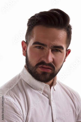Closeup portrait of handsome hipster man looking at camera in studio. Serious young man in white shirt posing isolated on white background.