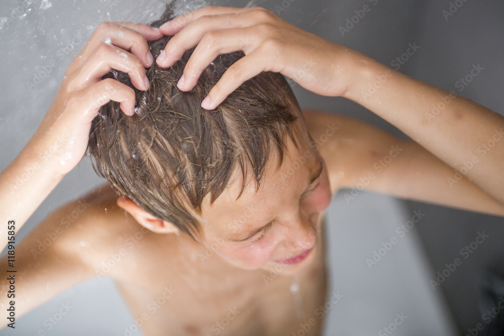 Naklejka premium Happy teen boy washing head in shower in the bathroom