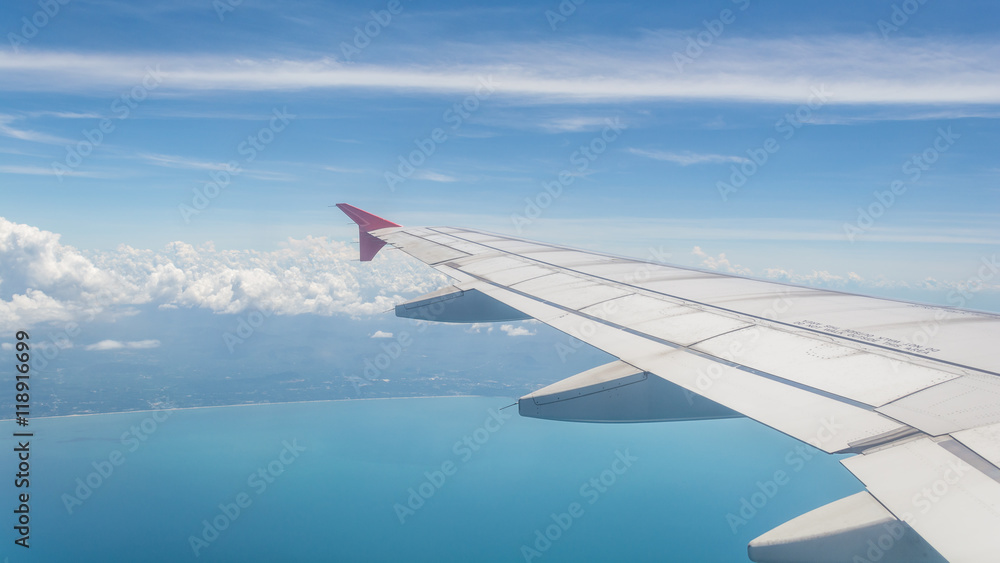 Fototapeta premium Wing of a plane from window view with bright blue sky and sea background.