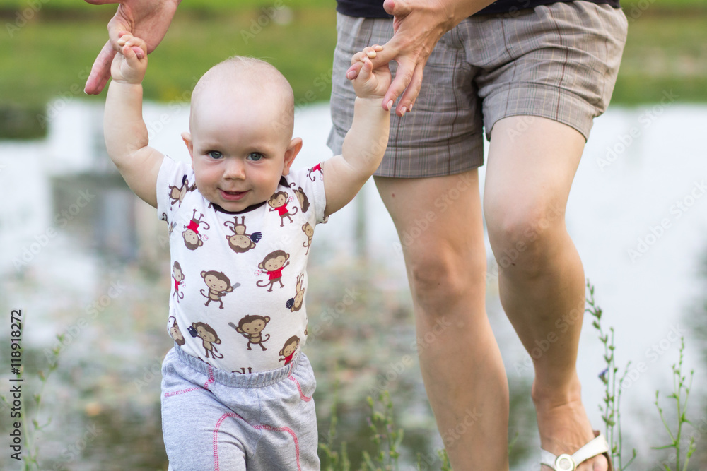 First Steps baby boy with mother in the park. Around a lot of green grass and trees in the summer. First Steps baby boy with mother in the park. Around a lot of green grass and trees in the summer.