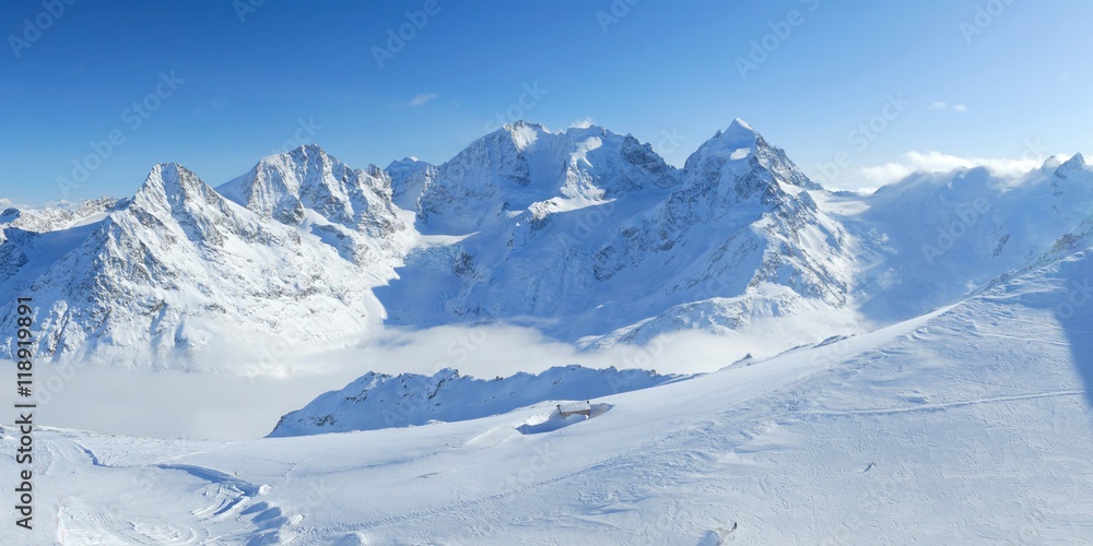 Winter mountains panoramic view with clouds in the valley and small hut. Corvatsch, Engadin, Switzerland.