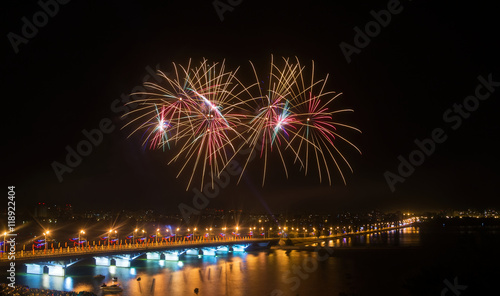 Fireworks over the city in large river with bridge in lights