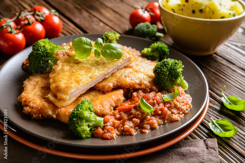 Piccata - fried pork cutlets stuffed with smoked ham slices coated in cheese and eggs served with tomato sauce, steamed broccoli and boiled potatoes