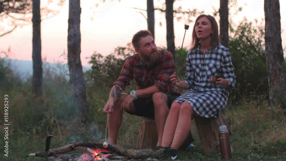 Young couple on a date in the forest to roast marshmallows in the fire Young couple on a date in the forest to roast marshmallows in the fire