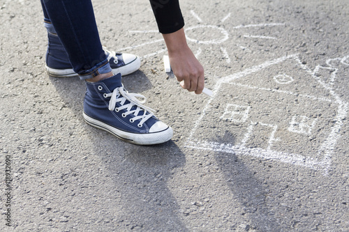 Girl draws by a chalk picture House and the Sun on asphalt 