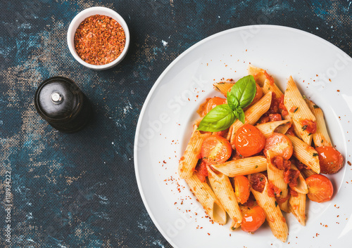 Pasta penne with tomato sauce, basil and roasted tomatoes. Old painted dark plywood background, top view, copy space, horizontal composition
