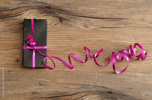 A black gift box decorated with a pink ribbon isolated on a wood