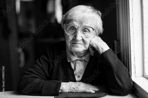 Elderly woman in glasses sitting at the table. Black and white photo.