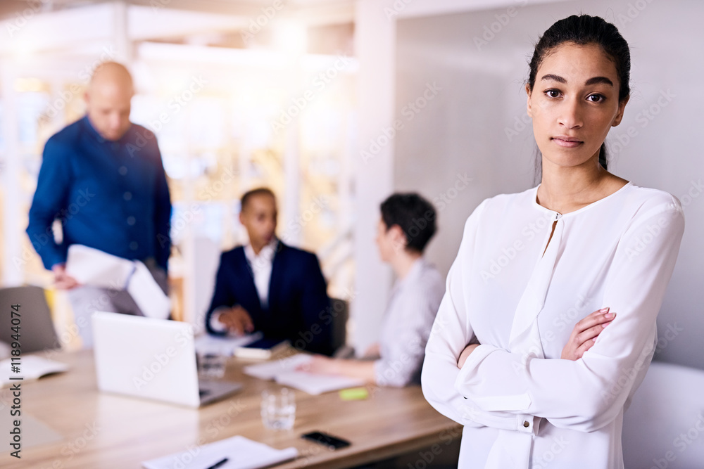 Young good looking mixed race business woman standing in front of three of her employees with her arms crossed while wearing a white blouse Young good looking mixed race business woman standing in front of three of her employees with her arms crossed while wearing a white blouse