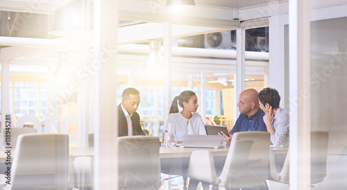 Corporate business meeting in modern office with glass walls, flare from the sunlight and reflections on the glass while business discussions take place amongst board members.