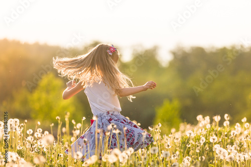 Obraz na plátně Girl running on the field of dandelions on summer sunset