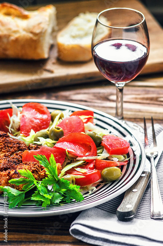 Homemade Breaded German Weiner Schnitzel and fresh vegetable spring salad with tomato  green olives  cabbage and parsley in white bowl on wooden table  closeup.