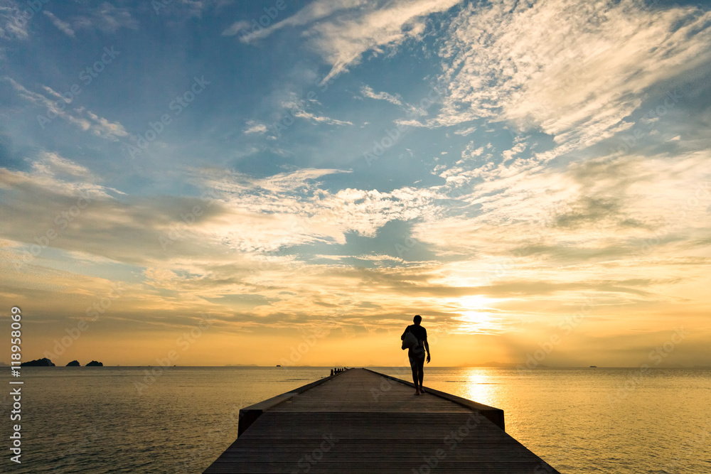 Man walks along the pier at sunset over the sea
