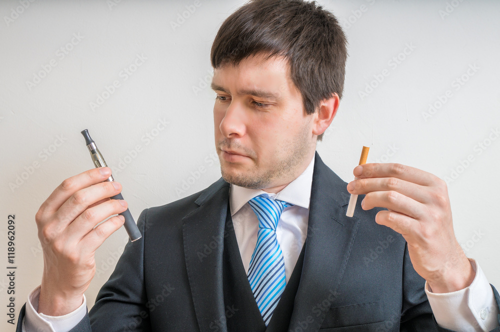 Man (smoker) is comparing classic tobacco cigarette and electronic vaporizer. Man (smoker) is comparing classic tobacco cigarette and electronic vaporizer.
