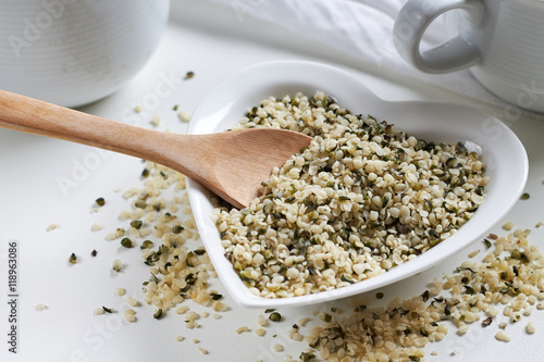 Hemp seeds in heart shaped ceramic bowl and wooden spoon on white background