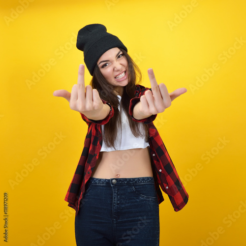 Hipster girl in jeans, checked shirt and hat showing middle fing