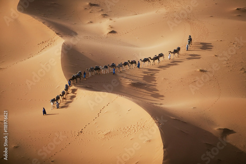 The setting sun over the desert makes a enchanting shadow as a caravan of camel merchants winds their way toward the next stop on their journey. photo