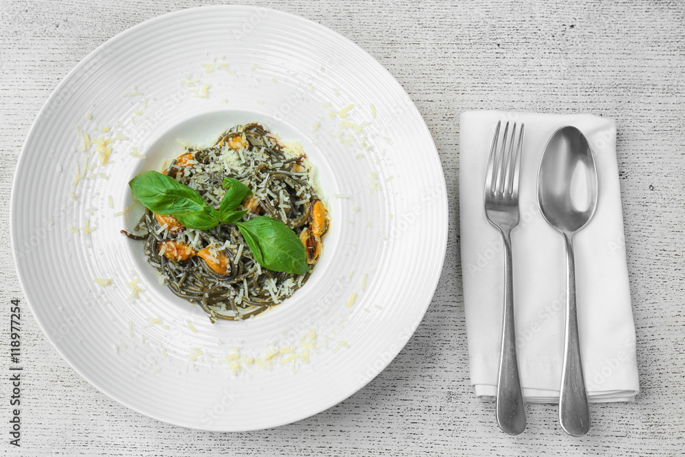 Plate with black spaghetti, mussels and cheese on white wooden table Plate with black spaghetti, mussels and cheese on white wooden table