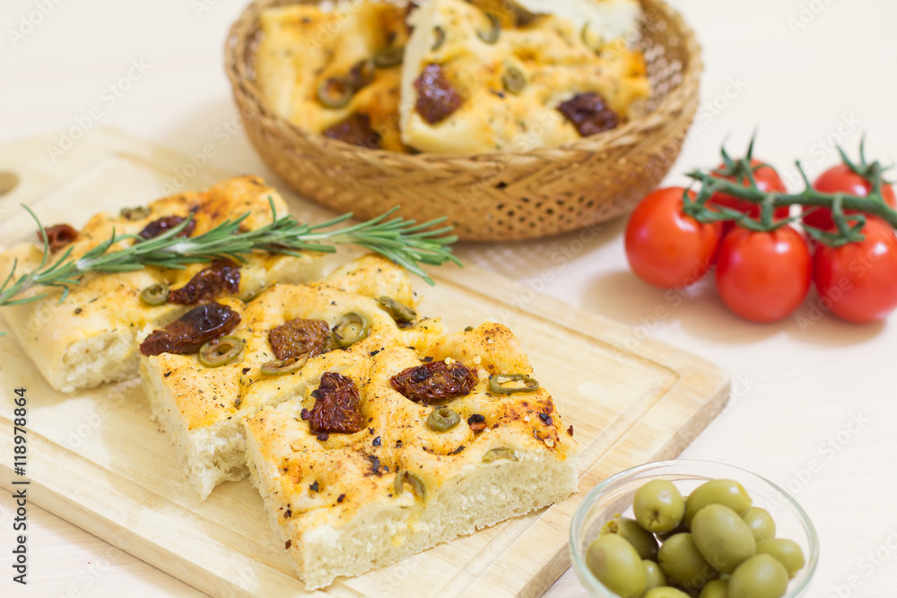 Freshly baked traditional Italian focaccia bread with green olives and sun-dried tomatoes, selective focus