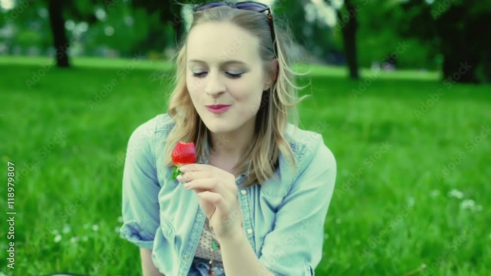 Happy girl sitting on the meadow in the park and eating strawberry
Happy girl sitting on the meadow in the park and eating strawberry