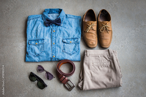 Men's casual outfits, jean shirt with bow tie, brown pants, sunglasses and shoes on gray background, flat lay