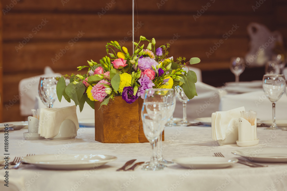 flower composition in wooden vase on the served table in the restaurant. Wedding dinner flower composition in wooden vase on the served table in the restaurant. Wedding dinner