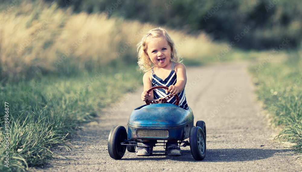 Spazierfahrt mit dem Tretauto, kleines Mädchen spielt draußen Spazierfahrt mit dem Tretauto, kleines Mädchen spielt draußen
