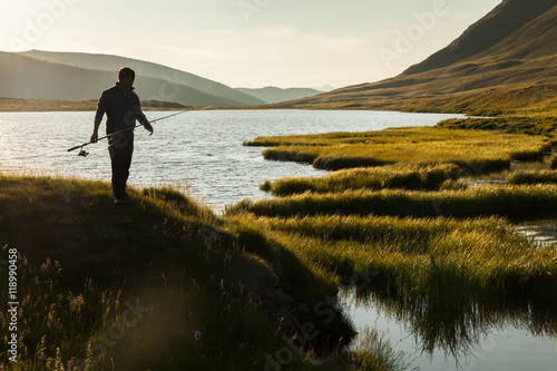 Silhouette of a fisherman with a fishing rod on the background o