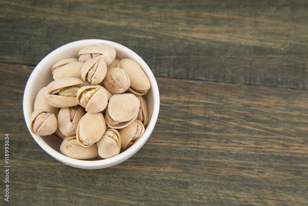 White bowl of pistachios on wooden background White bowl of pistachios on wooden background