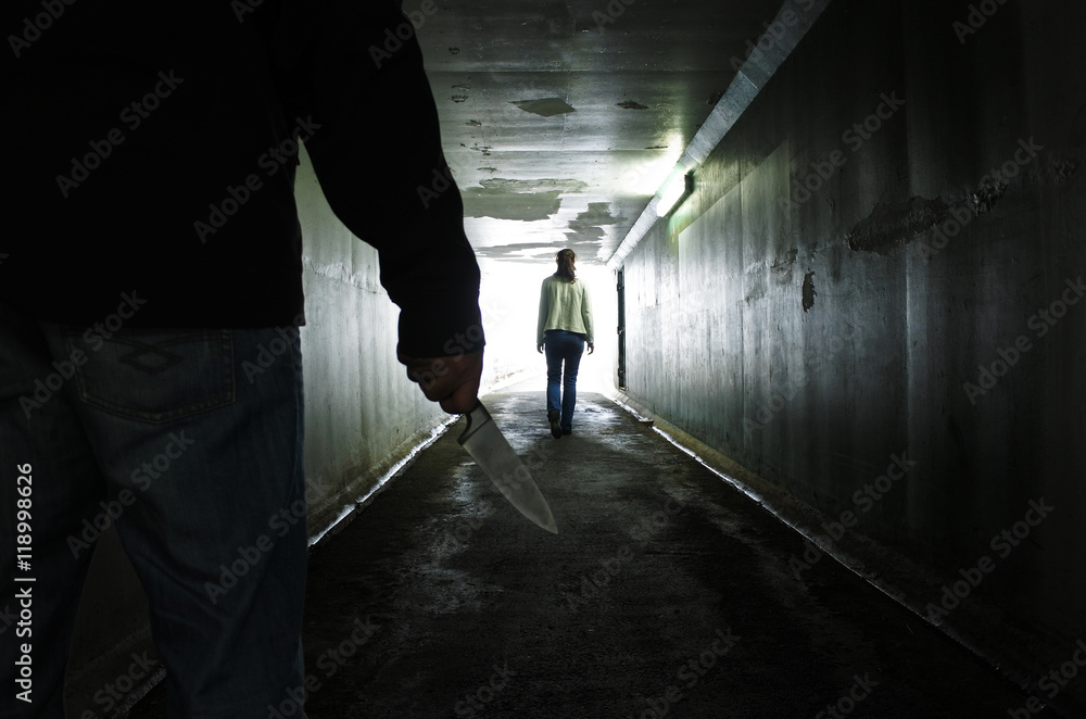 Man carries a knife follows a young woman in a dark tunnel