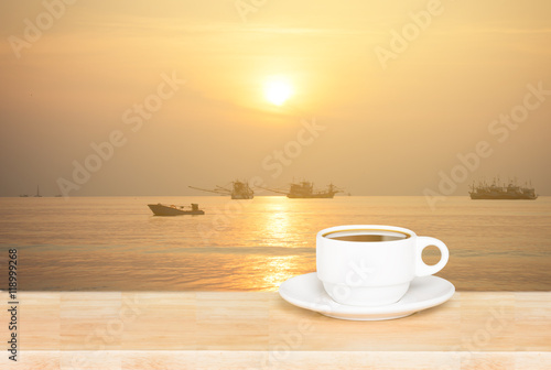 white coffee cup on wood table and view of sunset in the river background