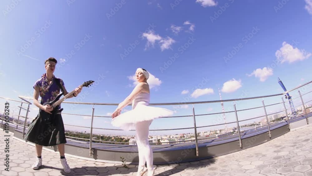 Man in skirt play electric guitar on seafront, sing in camera. Girl dance in ballerina suit. Crazy style Man in skirt play electric guitar on seafront, sing in camera. Girl dance in ballerina suit. Crazy style