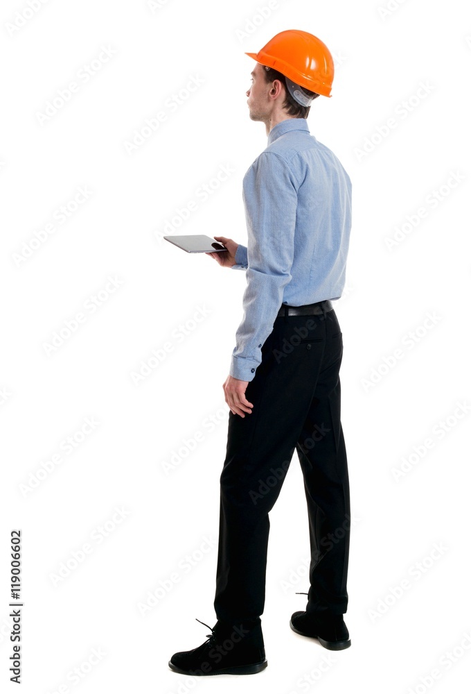 Backview of business man in construction helmet stands and enjoys tablet or using a mobile phone. Curly businessman in a light jacket and a helmet reads instructions from the tablet. Backview of business man in construction helmet stands and enjoys tablet or using a mobile phone. Curly businessman in a light jacket and a helmet reads instructions from the tablet.