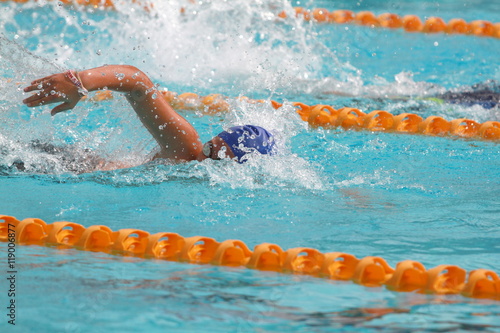 Young swimmer wearing blue cap practice freestyle stroke in a swimming pool for competition or race