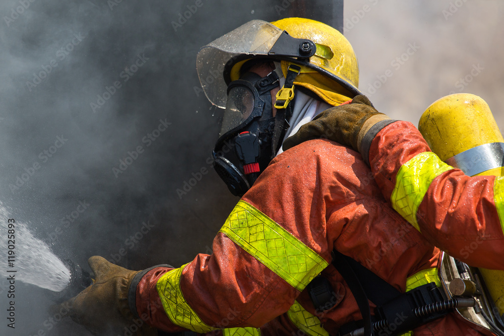 Fototapeta premium fireman in fire fighting suit spraying water to fire surround wi