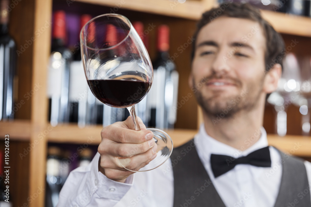 Young Bartender Examining Red Wine In Glass Young Bartender Examining Red Wine In Glass