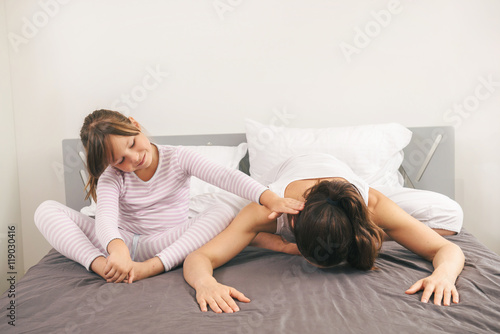 Mother with daughter doing yoga exercise in bed