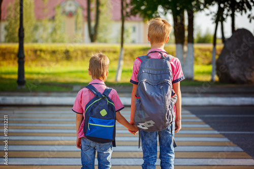 Two kids with backpacks walking on the road, holding. School tim photo