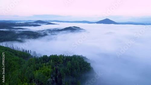 Time lapse. Hilly landscape after rainy night. Foggy valley bellow view point full of creamy mist. The fog is moving over treetops of forest. First pink sunrays of daybreak colored sky. photo