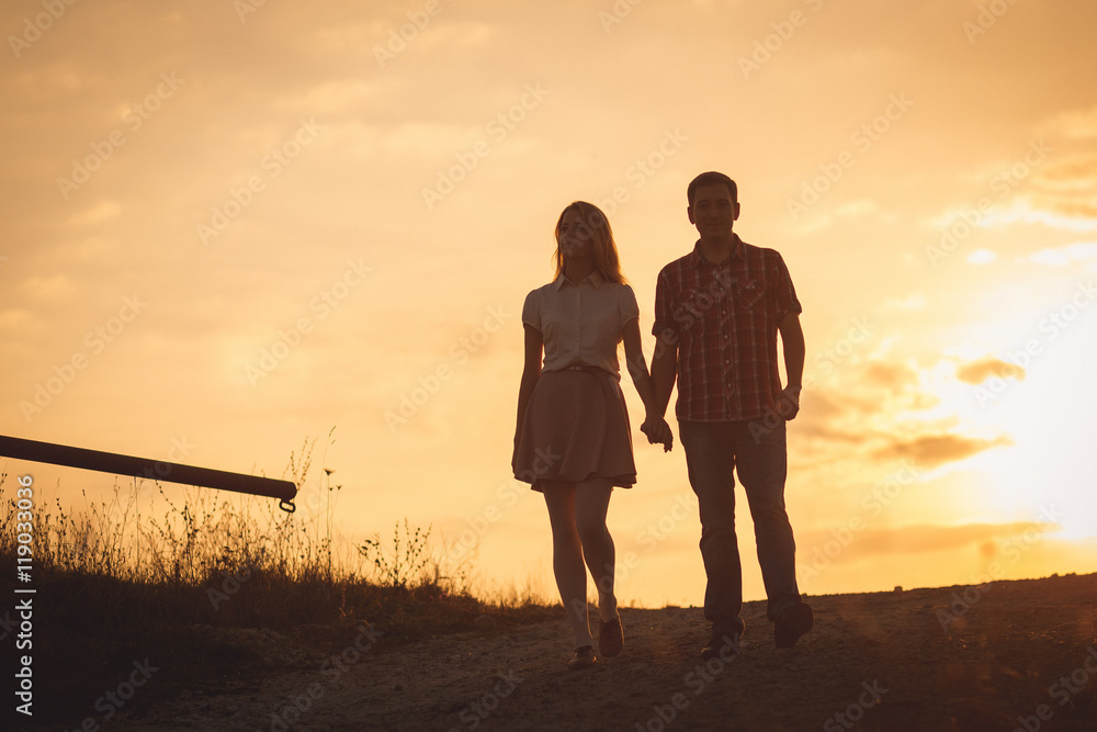 Golden sunset shines behind young couple holding their hands tog