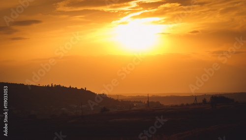 Golden sun illuminates sky over the dark field and village