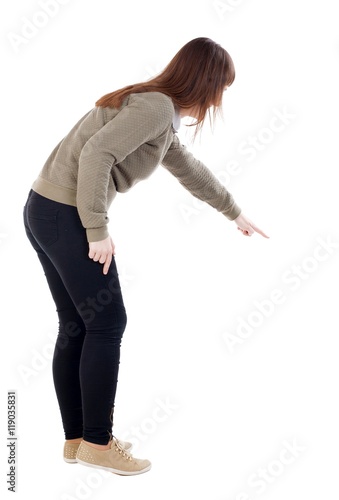 Back view of pointing woman. beautiful girl. Rear view people collection. backside view of person. Isolated over white background. A girl in a gray sweater shows finger of his right hand down