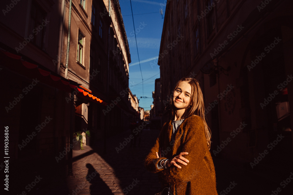 Shadows of evening town lie around young woman standing on the s