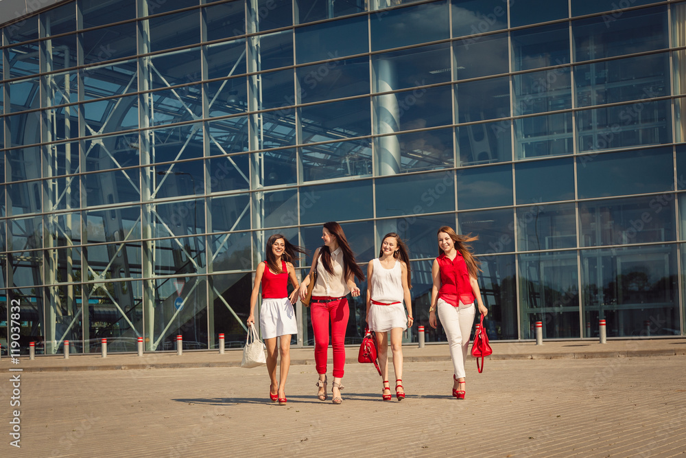 Wind blows hair of happy womans walking before large blue buildi