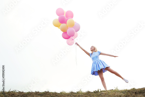 Beautiful young woman holding air balloons in field